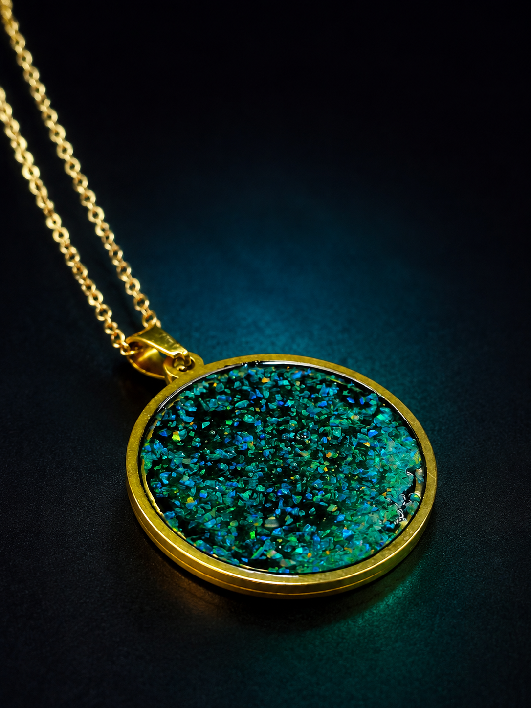 A gold pendant necklace featuring a round bezel-set iridescent stone with shimmering blue, green, and teal hues, displayed on a dark background.