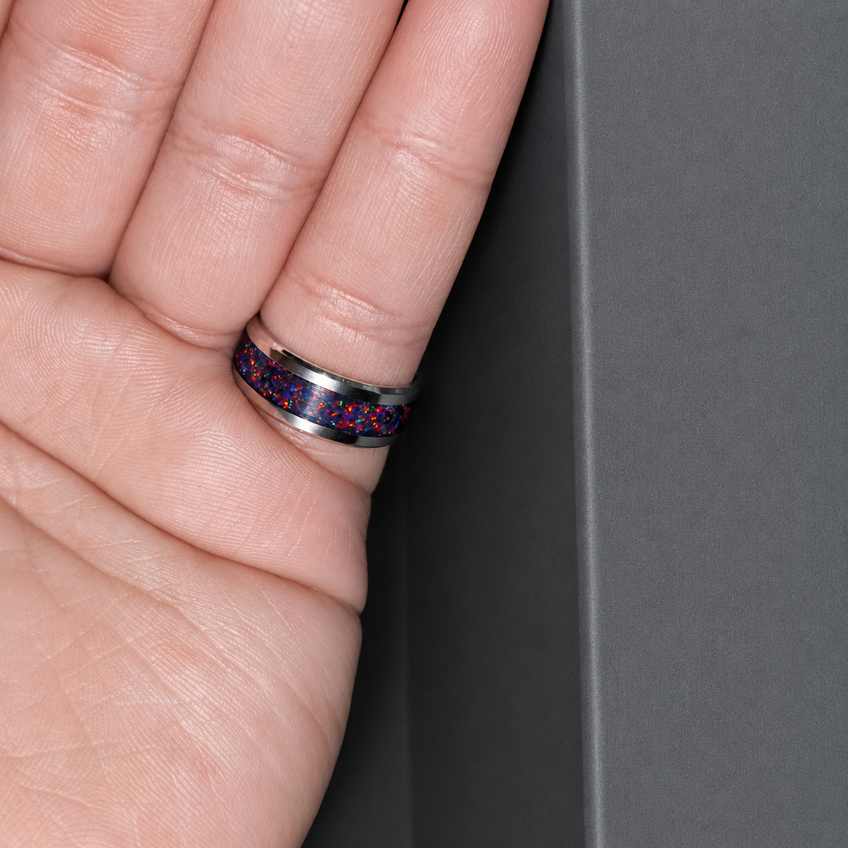 Close-up of a hand wearing a colorful ring on a gray background
